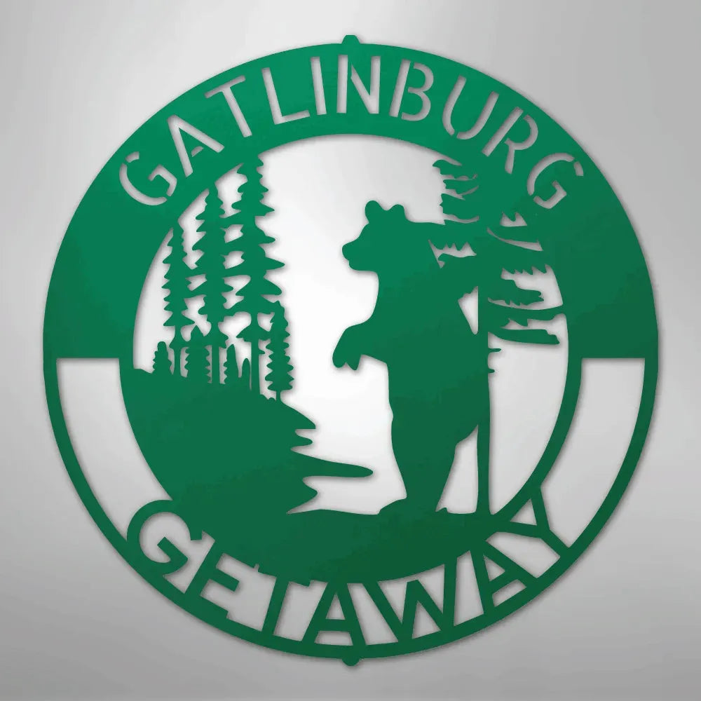 Green metal wall art: circular "Gatlinburg Getaway" sign with a bear and pine trees.