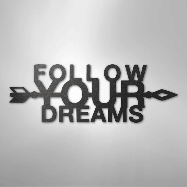 Black metal "Follow Your Dreams" wall art with an arrow design, casting a shadow on a light background.