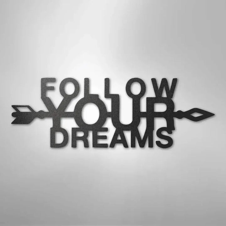 Black metal "Follow Your Dreams" wall art with an arrow design, casting a shadow on a light background.