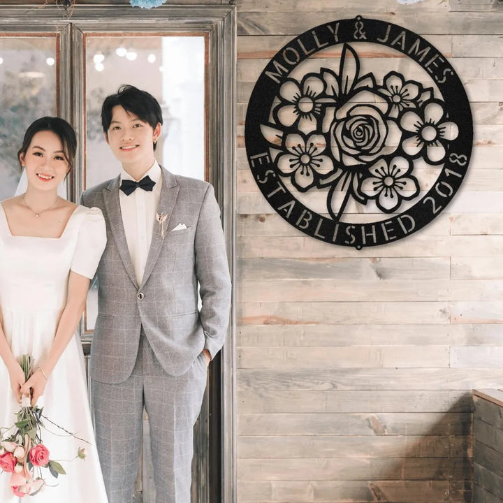 Black metal floral ring monogram wall art with "Molly & James Established 2018" on a wooden wall.