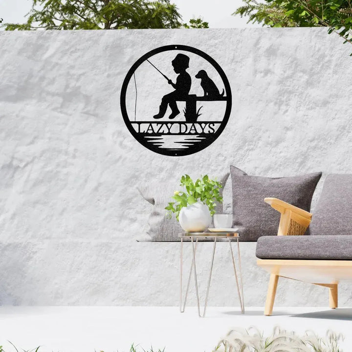 Black metal wall art: boy fishing with dog, "LAZY DAYS" text, circular design.