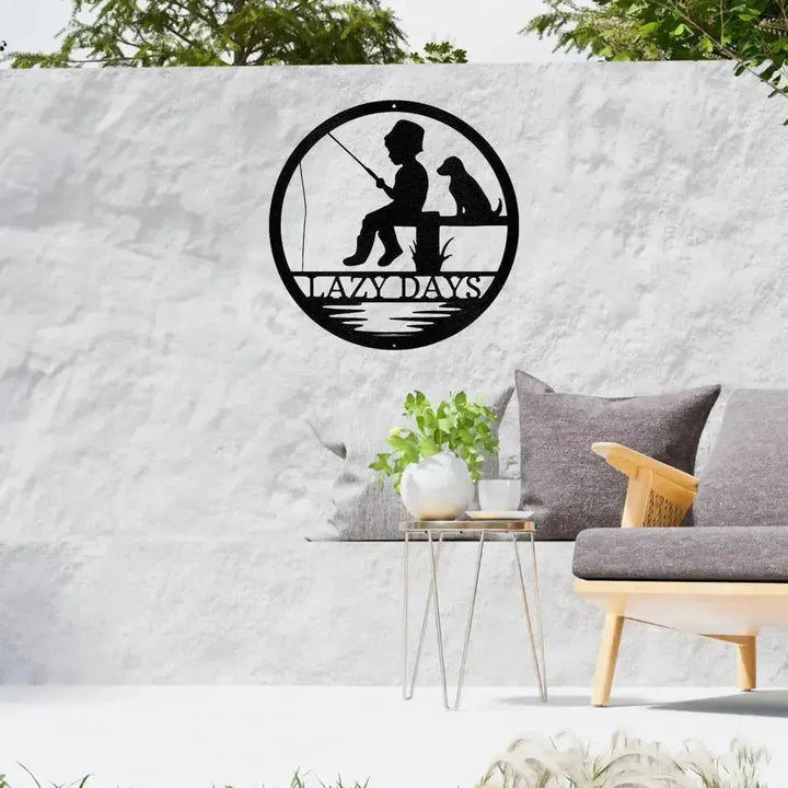 Black metal wall art: boy fishing with dog, "LAZY DAYS" text, circular design.