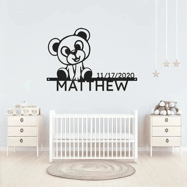 Black metal wall art featuring a teddy bear, "MATTHEW", and a birthdate above a white crib.