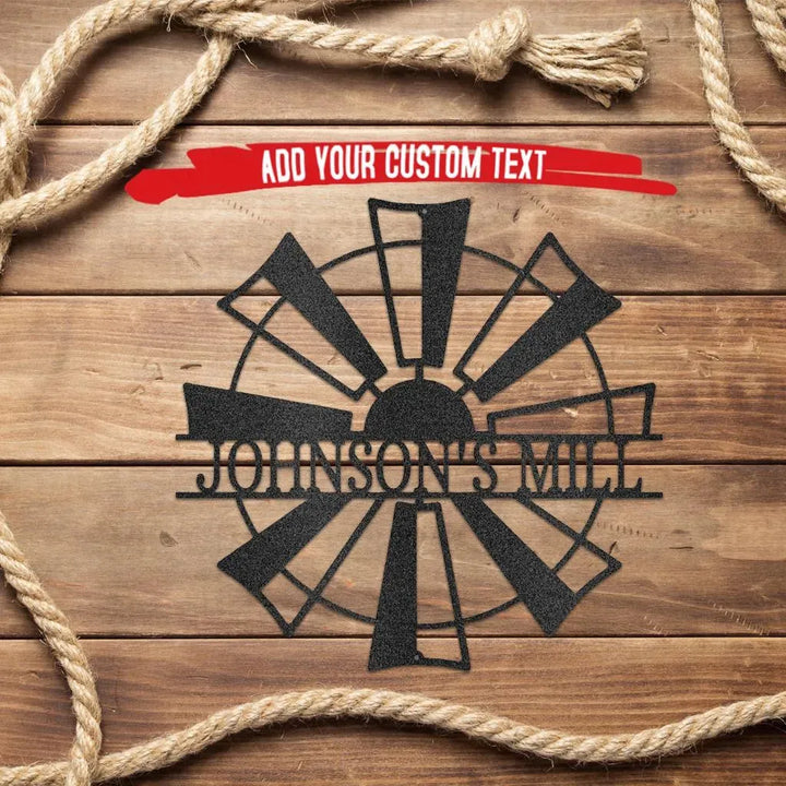 Black metal windmill monogram wall art with "JOHNSON'S MILL" text on a wooden background with rope.