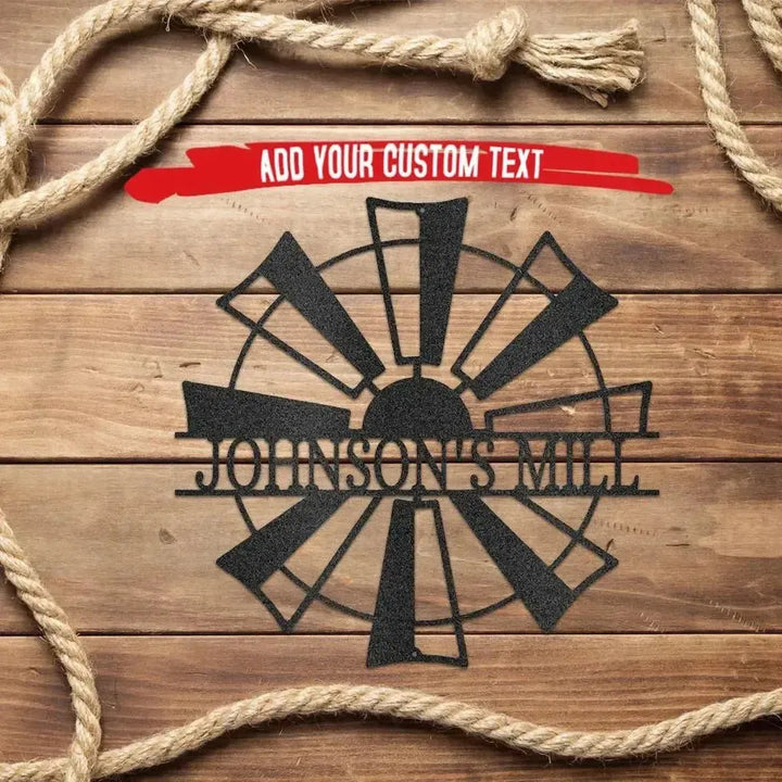Black metal windmill monogram wall art with "JOHNSON'S MILL" text on a wooden background with rope.