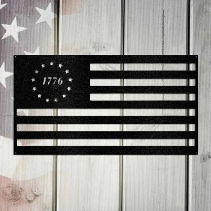 Black metal 1776 flag wall art with 13 stars in a circle, mounted on a rustic wooden background.