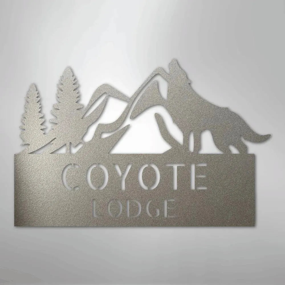 Gray metal wall art featuring a howling coyote, mountains, pine trees, and "COYOTE LODGE" text.