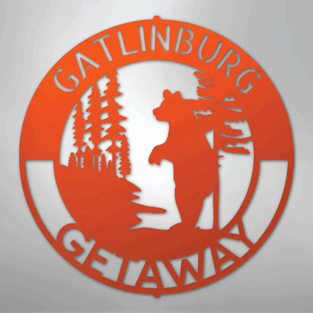 Orange metal wall art with "Gatlinburg Getaway" text, a bear, and pine trees in a circular design.