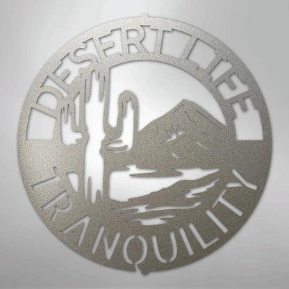 Circular silver metal wall art with "DESERT LIFE TRANQUILITY" text, saguaro cactus, and mountain design.
