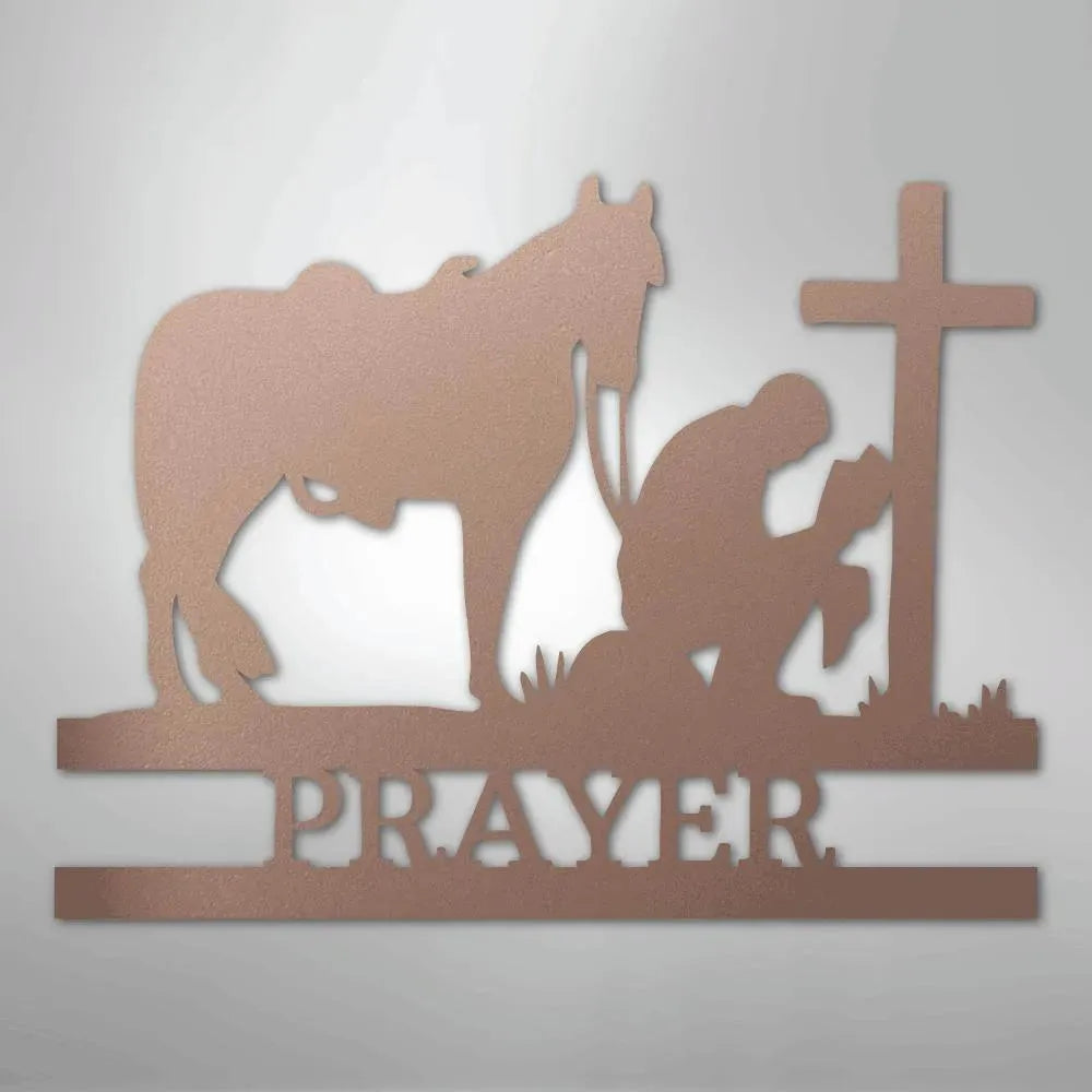 Bronze metal wall art of a cowboy kneeling by a cross and horse, with "PRAYER" cut out below.