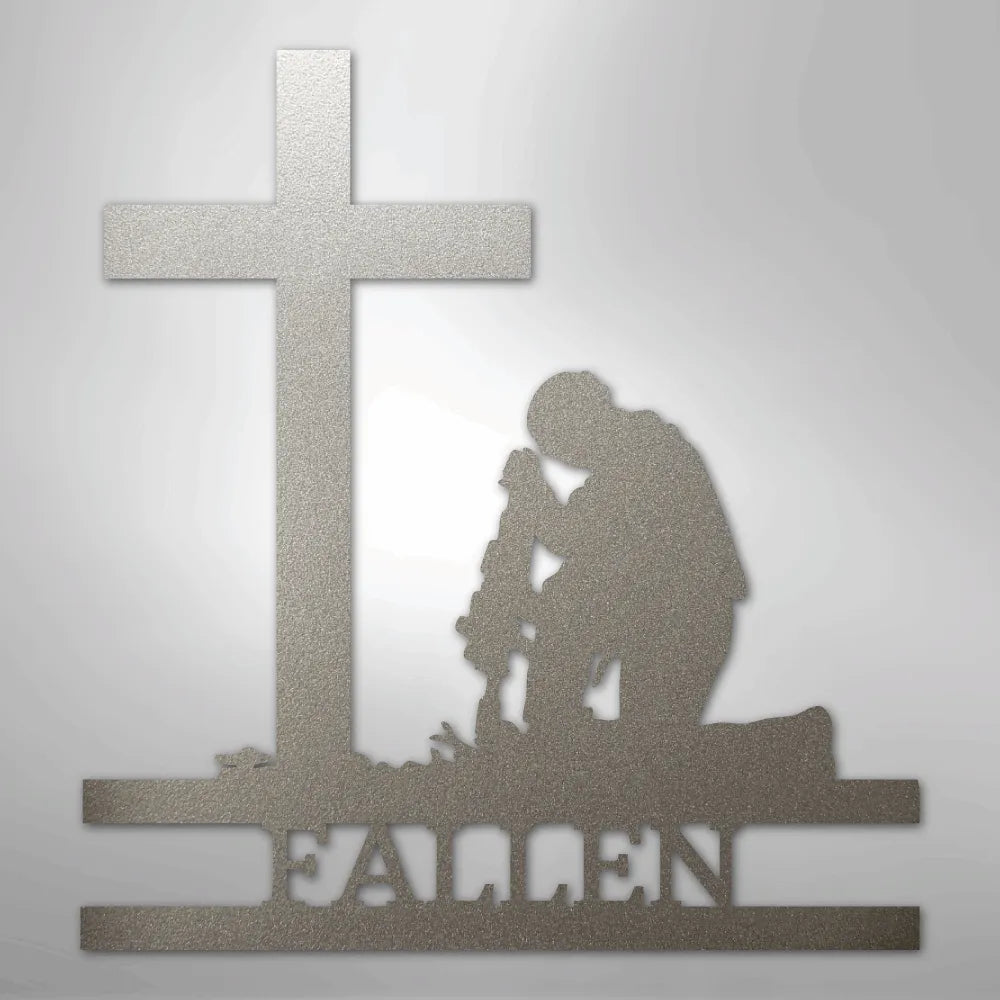 Silver metal wall art of a kneeling soldier silhouette before a cross, with "FALLEN" cut out below.