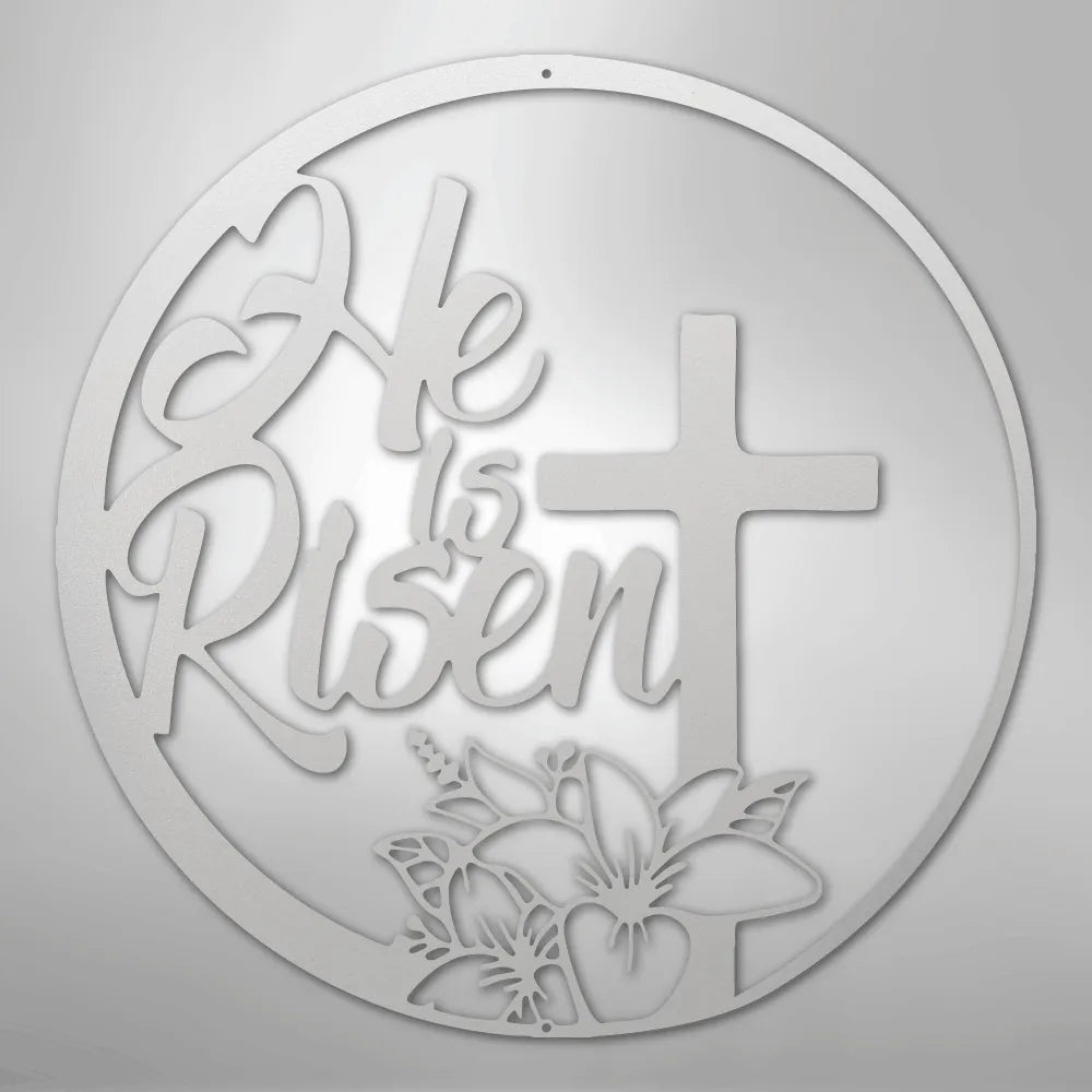 White "He is Risen" metal wall art with a cross and lily design in a circular frame.