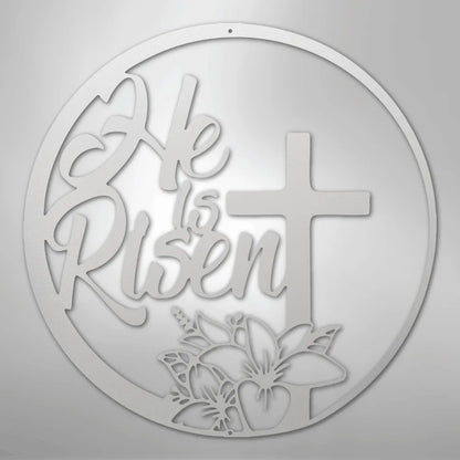 White "He is Risen" metal wall art with a cross and lily design in a circular frame.