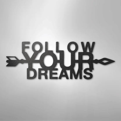 Black metal "Follow Your Dreams" wall art with an arrow design, casting a shadow on a light background.