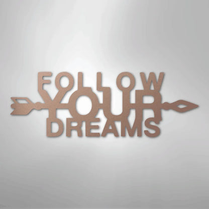 Copper metal wall art spelling "FOLLOW YOUR DREAMS" with an arrow design, casting a shadow.