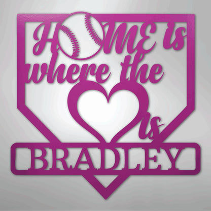 Pink metal baseball home plate sign with "Home is where the heart is" and "BRADLEY" cut out.