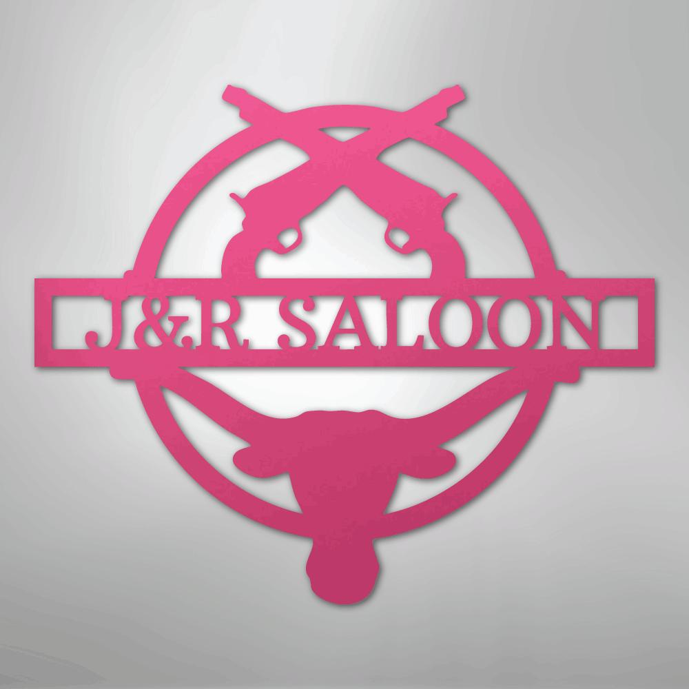 Pink metal "J&R Saloon" monogram with crossed pistols, a longhorn skull, and a circular border.
