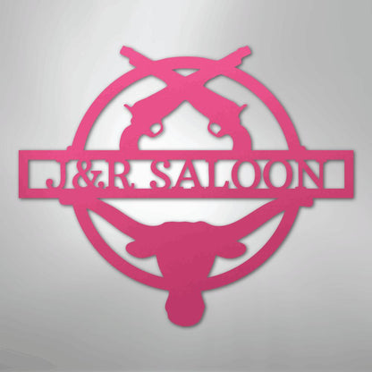 Pink metal "J&R Saloon" monogram with crossed pistols, a longhorn skull, and a circular border.