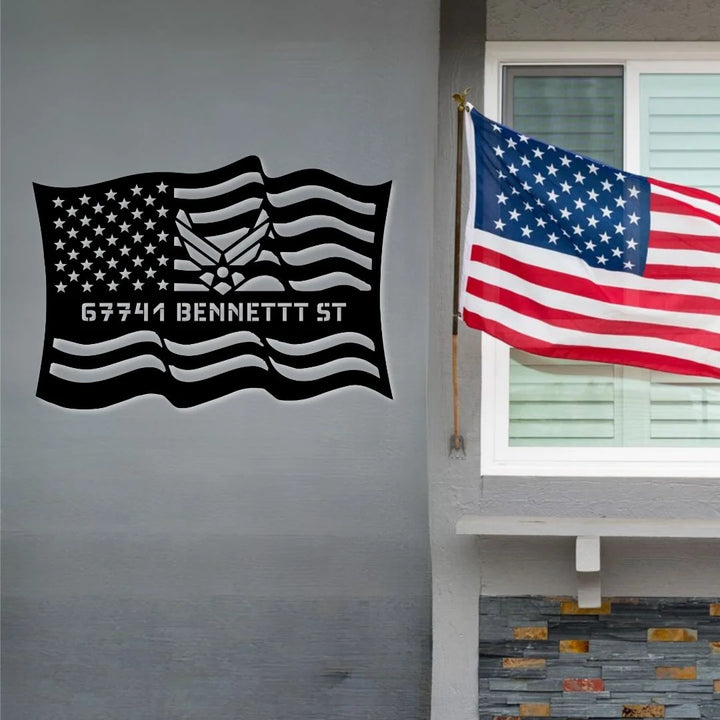 Black American flag design on a gray wall next to an American flag outside a building.