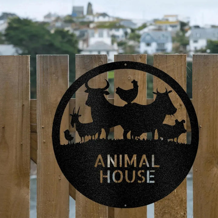 Black metal Animal House monogram with farm animals, hanging on a wooden fence outdoors.