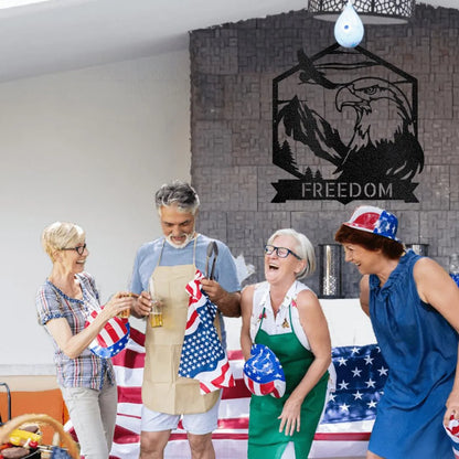 Black metal Bald Eagle Monogram wall art with "FREEDOM" banner, mounted on a stone wall above people celebrating.