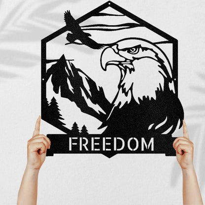 Black metal bald eagle monogram with mountains, trees, and "FREEDOM" text, held by hands.