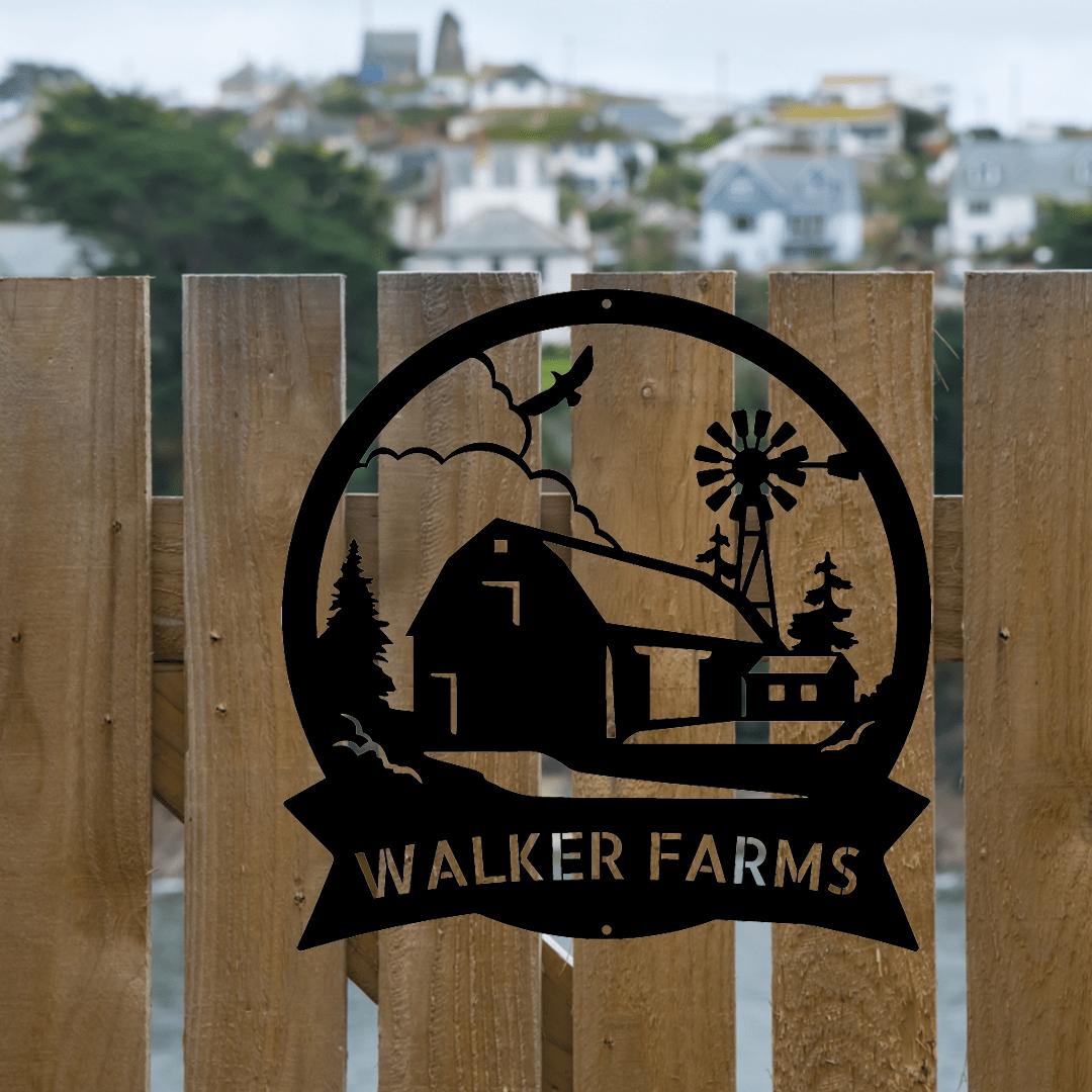 Black metal Barn House Monogram Wall Art with "WALKER FARMS" text, featuring a barn, windmill, and trees, hanging on a wooden fence.