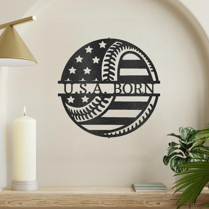 Black metal "U.S.A. BORN" wall art with baseball and American flag design, mounted on a light wall.