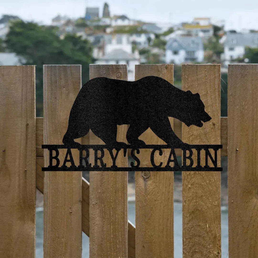 Black metal bear monogram wall art with "BARRY'S CABIN" text, mounted on a wooden fence.