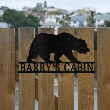Black metal bear monogram wall art with "BARRY'S CABIN" text, mounted on a wooden fence.