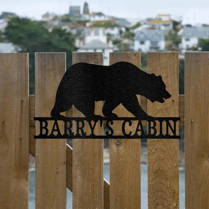 Black metal bear monogram wall art with "BARRY'S CABIN" text, mounted on a wooden fence.
