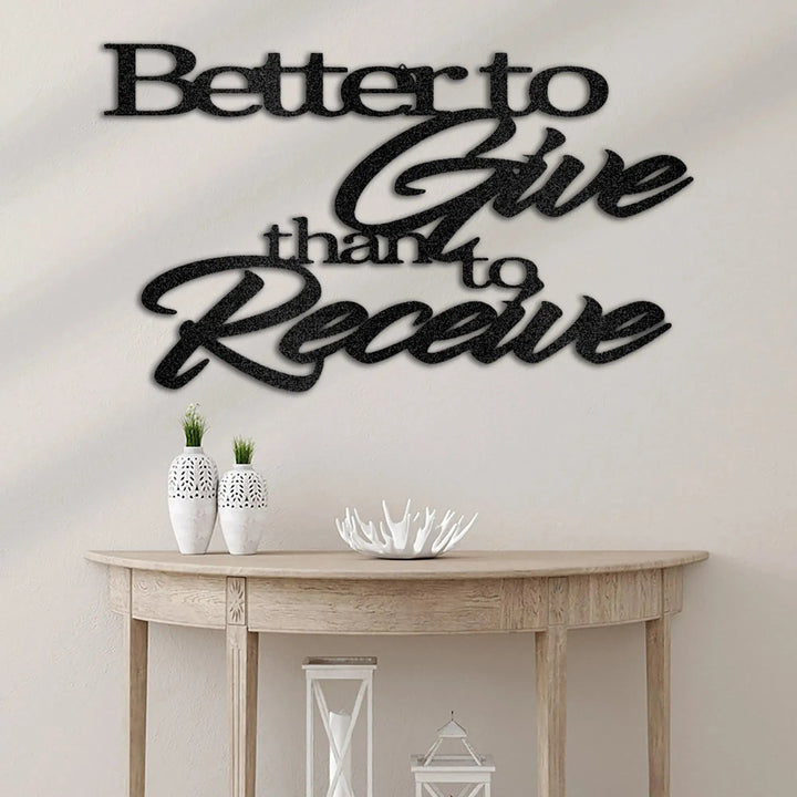 Black metal "Better to Give than to Receive" wall art above a wooden console table.