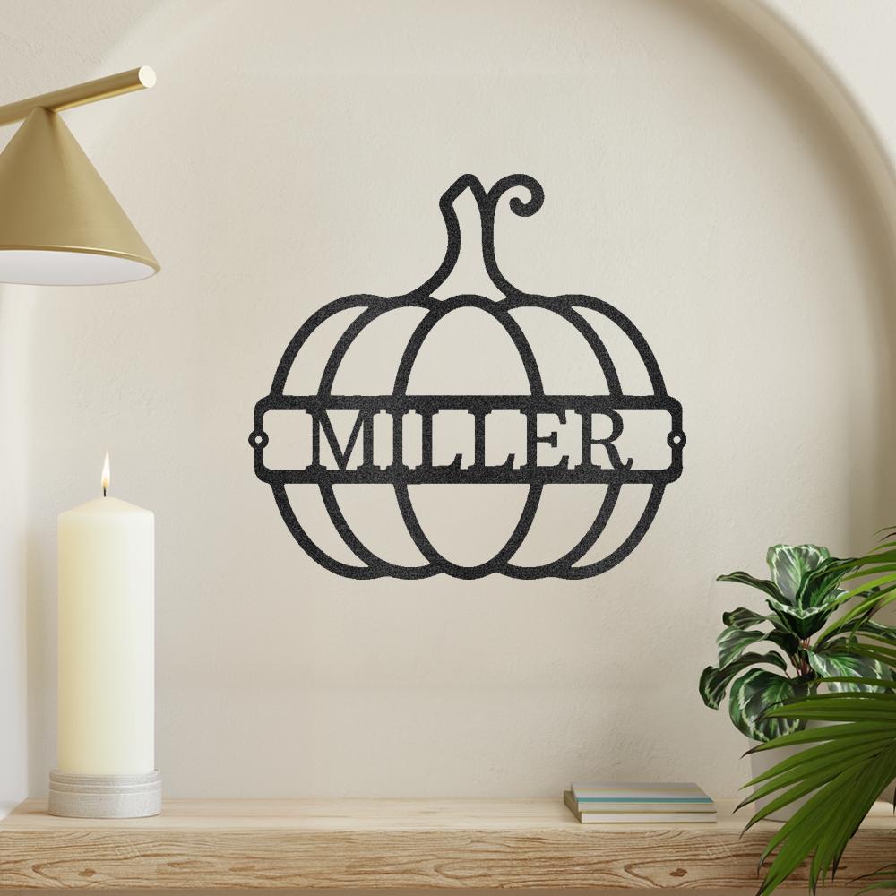 Black metal pumpkin wall art with "MILLER" cutout, displayed on a light wall above a candle and plant.