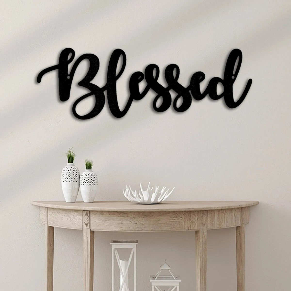 Black script metal wall art spelling "Blessed" in a flowing, elegant font above a wooden console table.