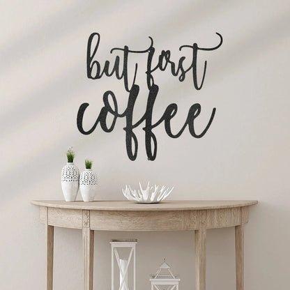 Black metal "but first coffee" script wall art above a light wood console table.