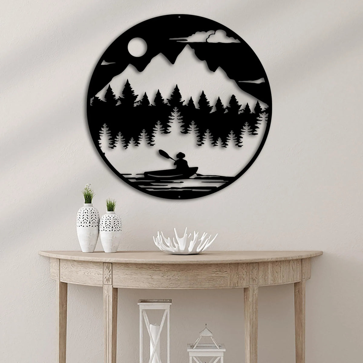 Black metal wall art: round wilderness scene with mountains, pine trees, moon, and a person kayaking.