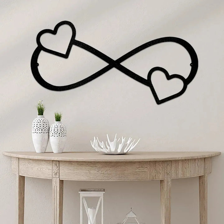 Black metal infinity symbol wall art with two hearts, one on each loop, mounted above a wooden console table.