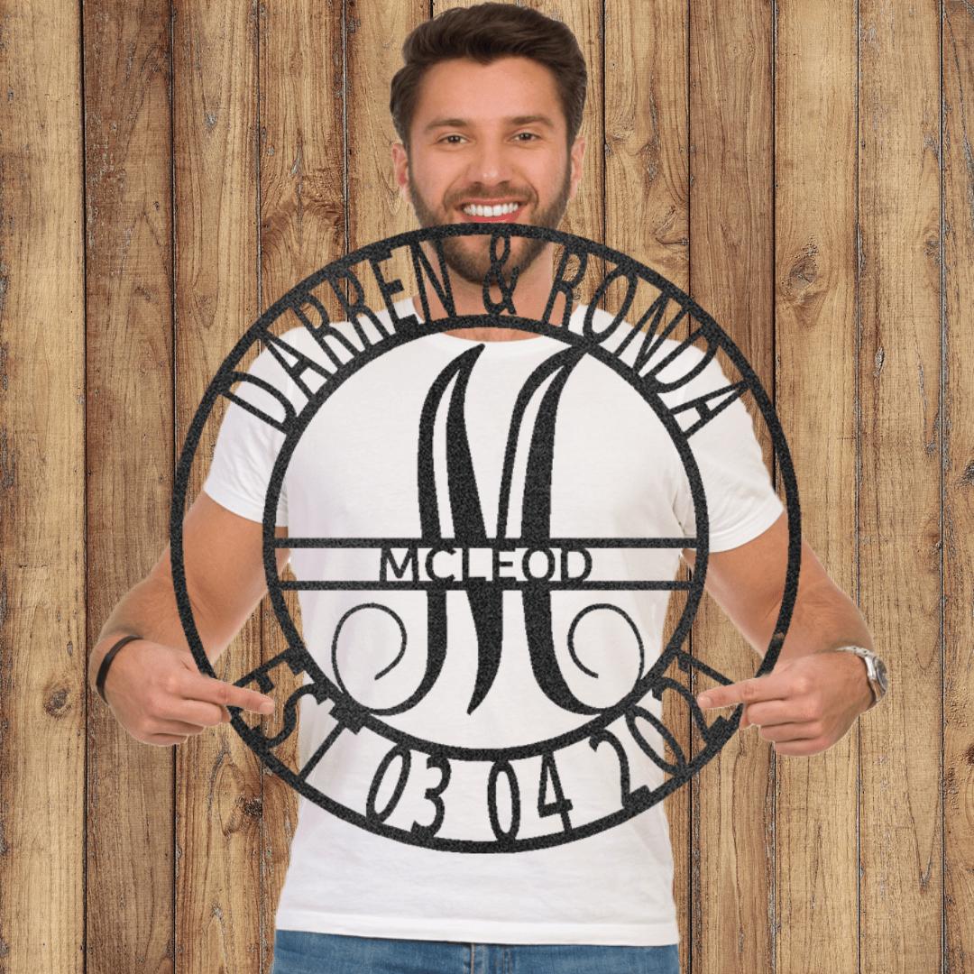 Man holding a round black metal family name sign with "Darren & Ronda," a large "M," and "McLeod 03 04 20" cut out.