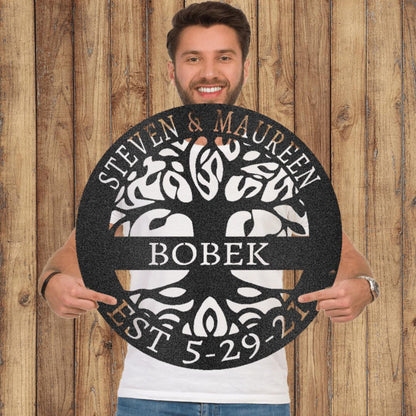 Man holding a round black metal Tree of Life wall art with personalized names and date.
