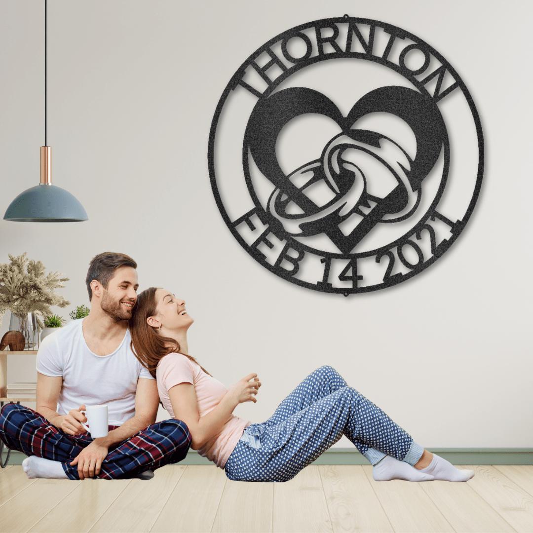Black metal wall art with "THORNTON FEB 14 2021" encircling a heart and intertwined rings.