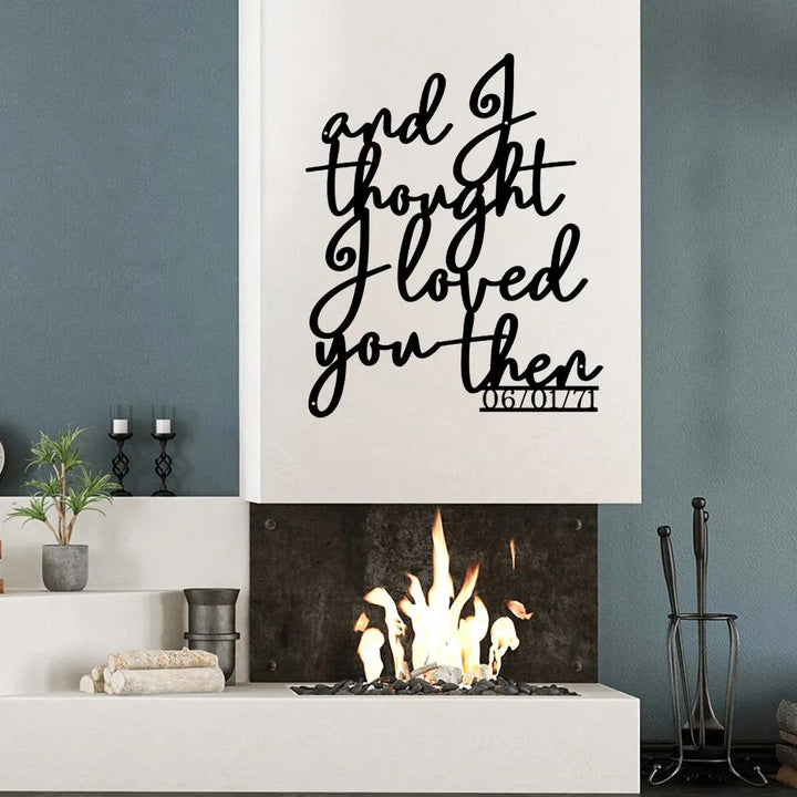 Black metal wall art with "and I thought I loved you then" script and a date, above a modern fireplace.