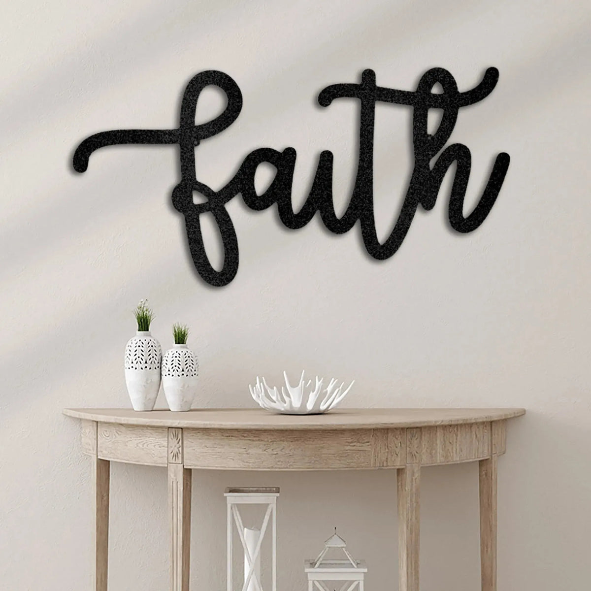Black script "faith" metal wall art mounted above a light wood console table with decor.