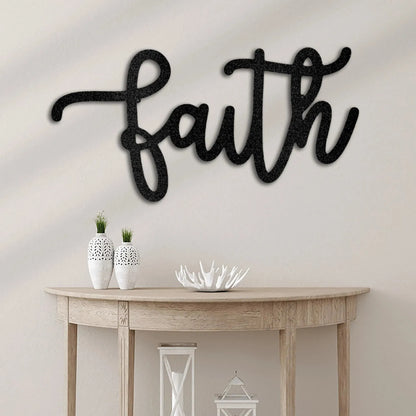Black script "faith" metal wall art mounted above a light wood console table with decor.