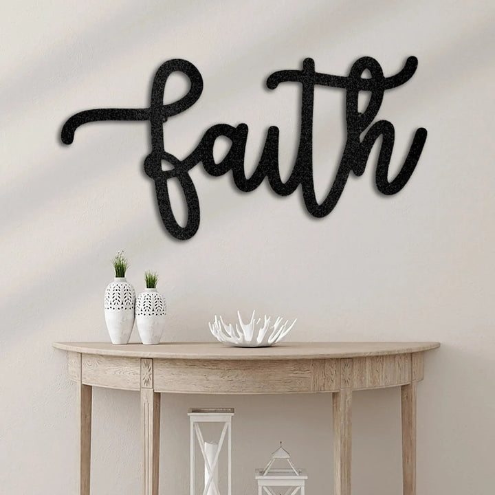 Black script "faith" metal wall art mounted above a light wood console table with decor.