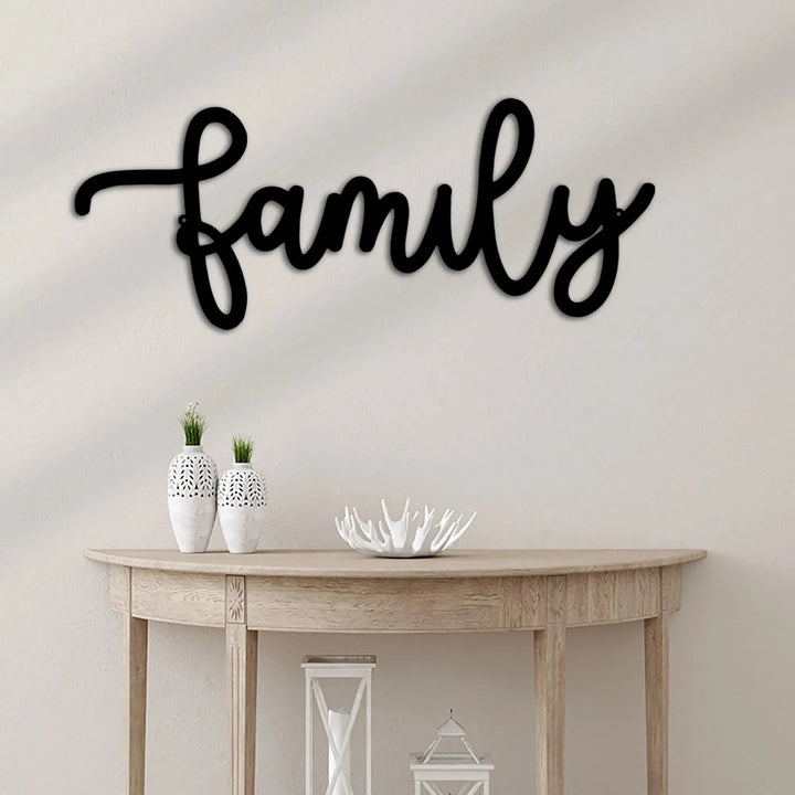 Black script "Family" metal wall art above a wooden console table with white vases.
