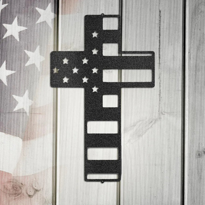 Black metal flag cross wall art with stars and stripes cutouts on a rustic wood background.