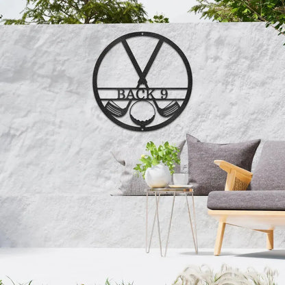 Black metal golf club monogram art with "BACK 9" text, golf clubs, and ball, on a white outdoor wall.