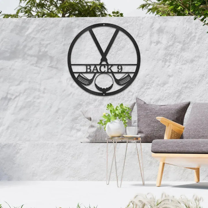 Black metal golf club monogram art with "BACK 9" text, golf clubs, and ball, on a white outdoor wall.