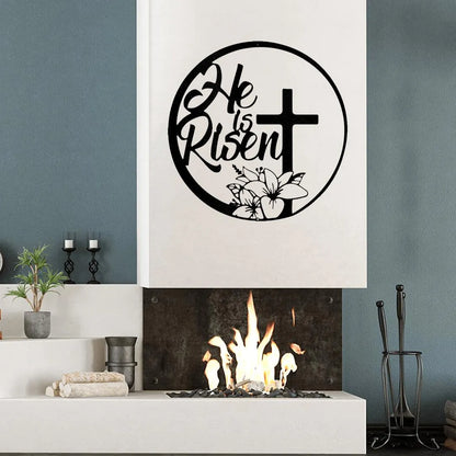 Black metal "He is Risen" wall art with a cross and lilies, displayed above a modern fireplace.