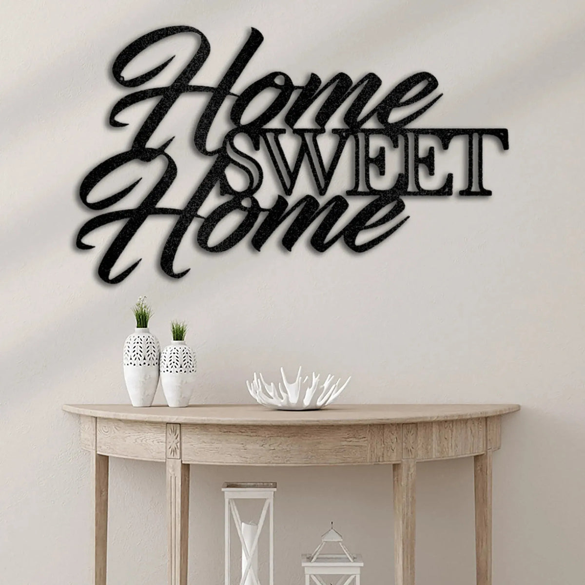 Black metal "Home Sweet Home" script wall art above a wooden console table with white decor.
